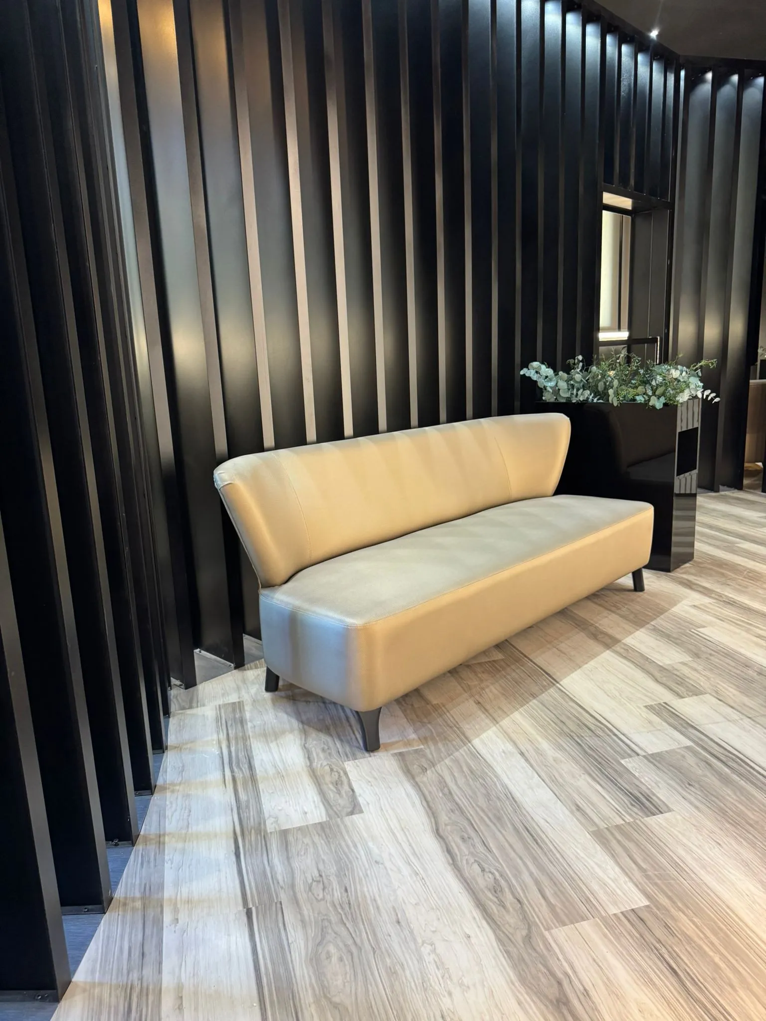 Banc d'entrada amb tapisseria crema sobre fons de paret de làmines negres.